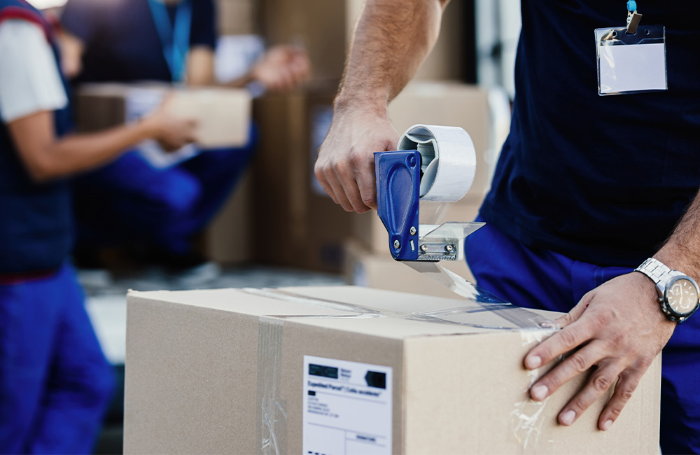 closeup delivery man closing carboard box with tape while preparing packages shipment Nakil Turk